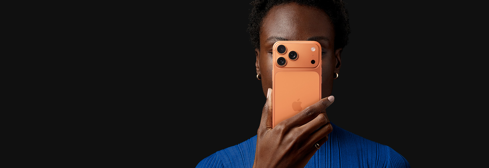 Une personne tient un iPhone 17 Pro devant son visage, face arrière tournée vers l’extérieur, coloris Orange Cosmique
