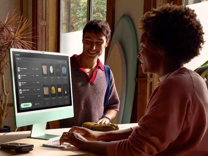 明るい部屋にいる2人の人物。そのうちの1人がグリーンのM4搭載iMac上で注文の支払い手続きをしている