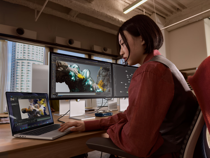 Person using MacBook Pro with two Studio Displays, seamlessly editing a digital art project.