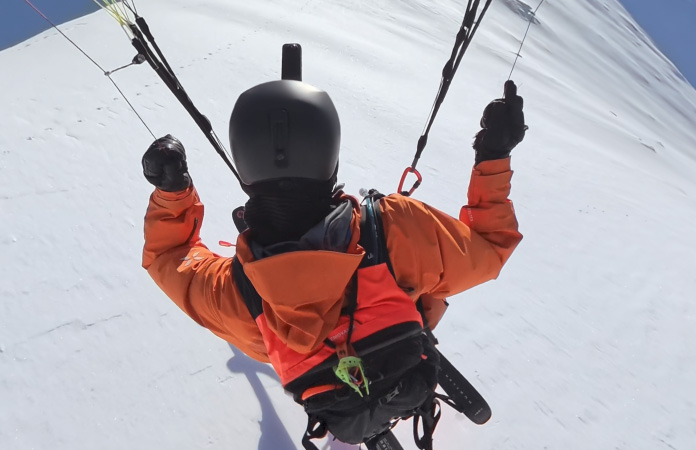 Someone paraskiing through air across sweeping mountaintop in wide field of view